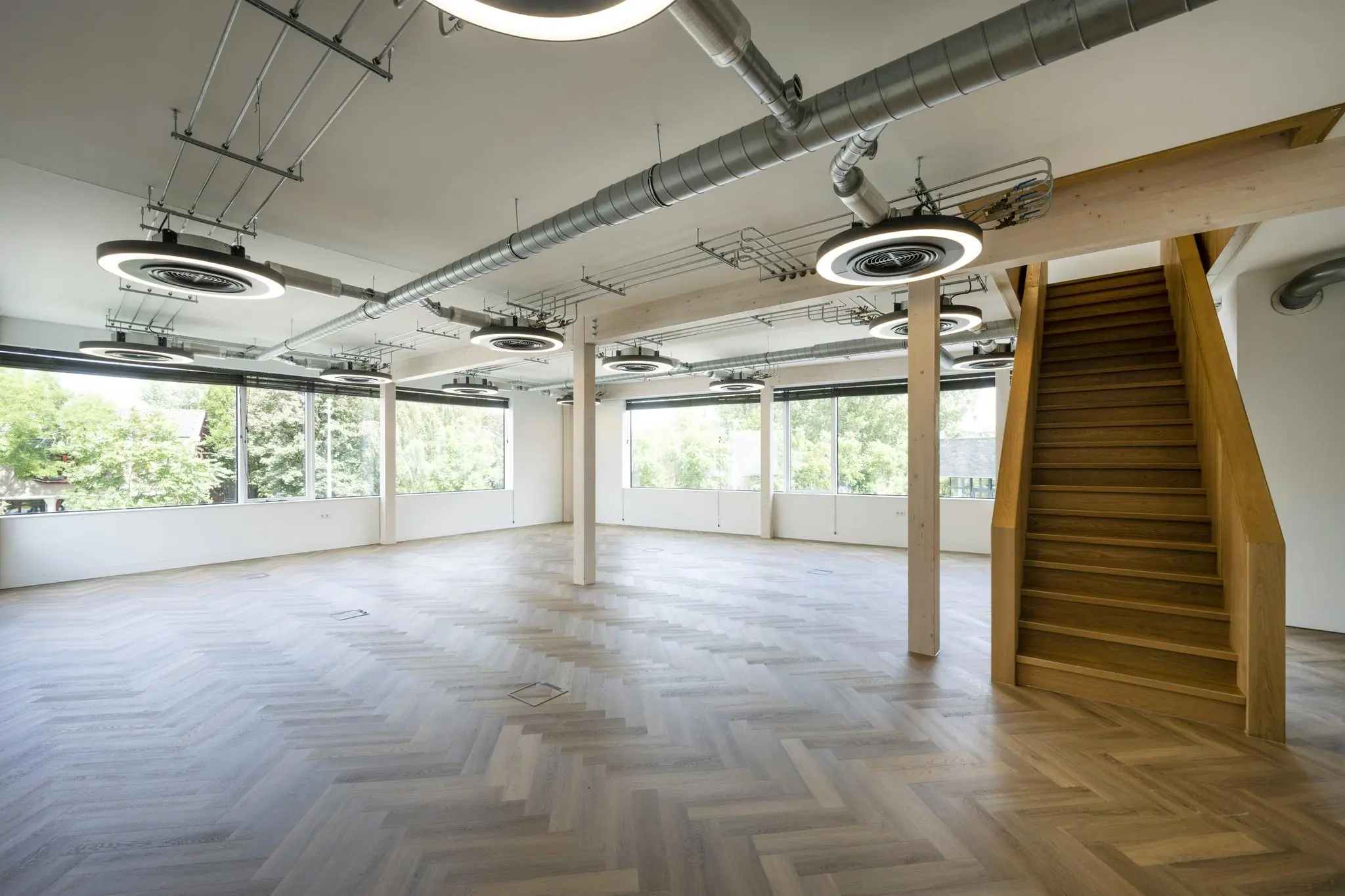 Licht en modern kantoorinterieur aan de Fred. Roeskestraat met visgraatvloer, houten trap en industriële plafonddetails.